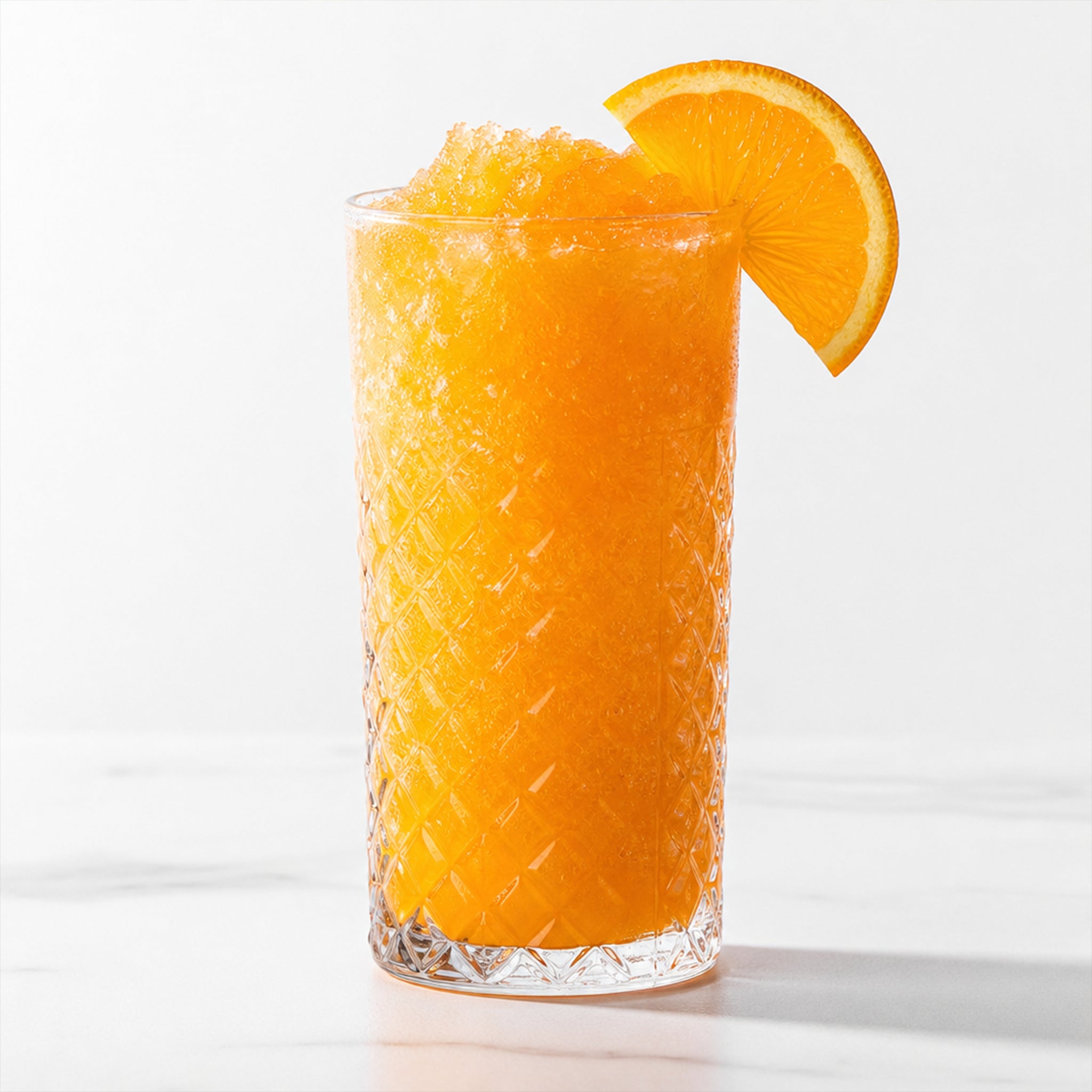 A tall textured clear glass filled with bright orange slushy or iced orange drink, garnished with an orange slice on a white background.