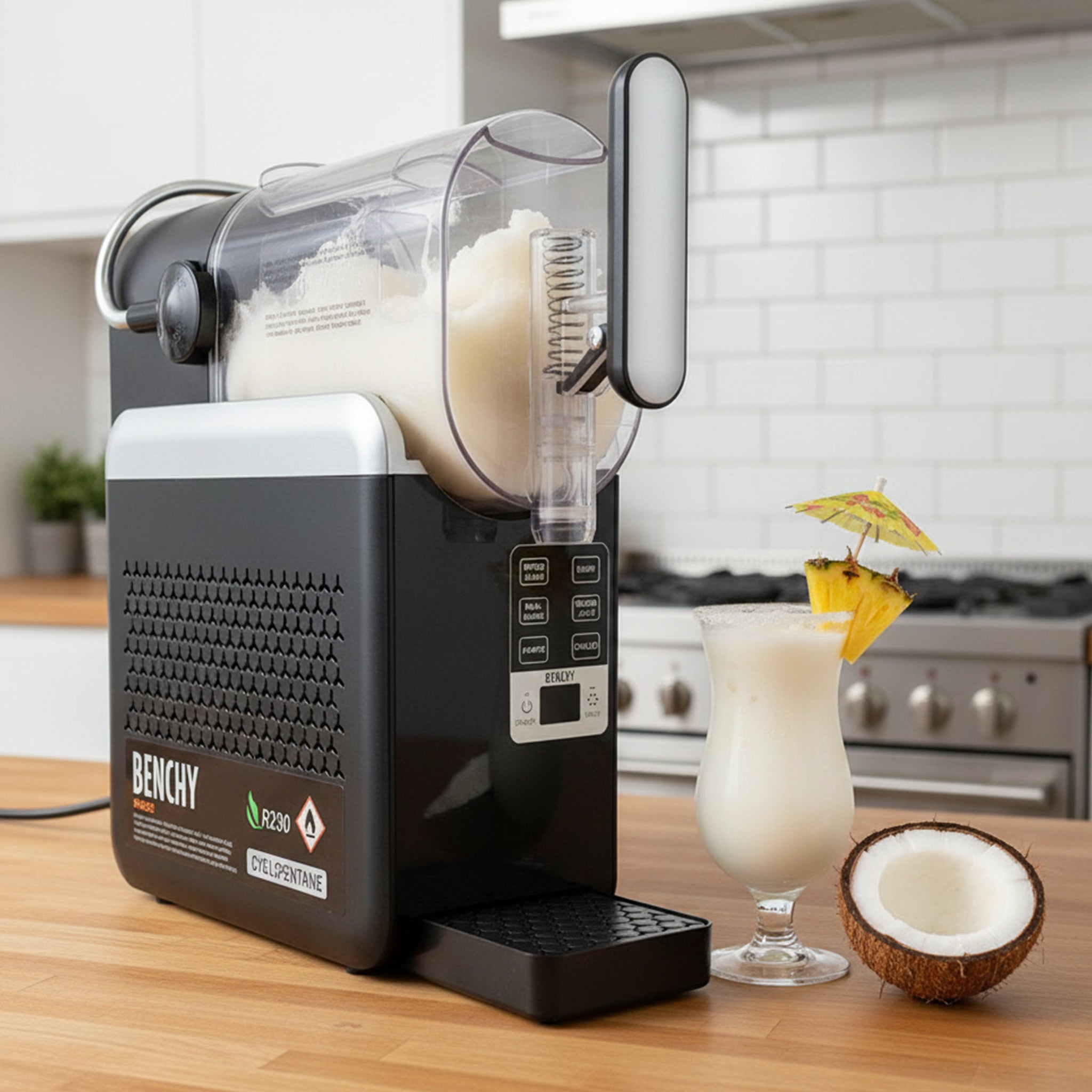 A BENCHY ice machine in a kitchen setting, shown dispensing a creamy white frozen drink into a tall glass. A coconut half and a cocktail umbrella sit beside the glass on the wooden counter.