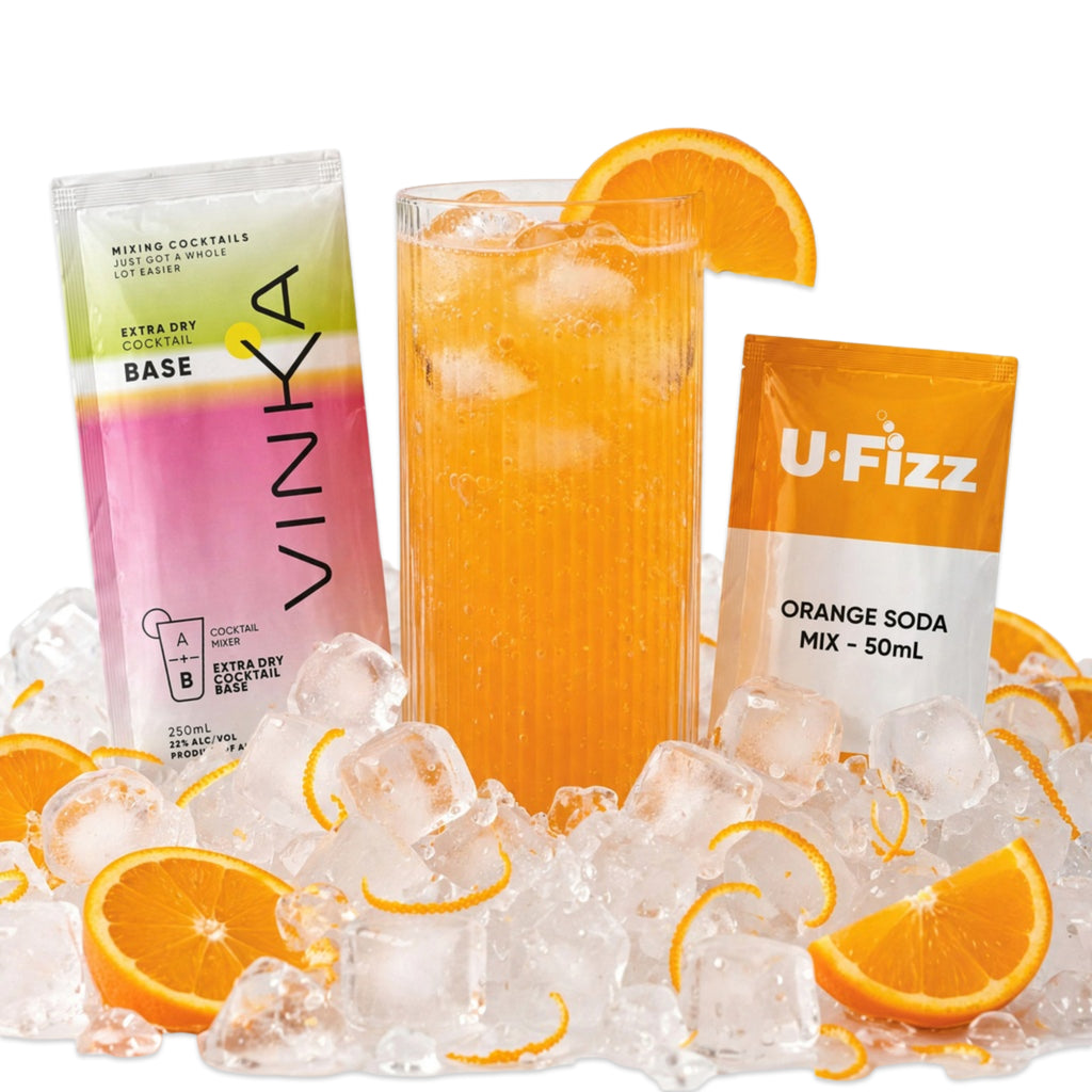 A Vinka cocktail base packet, a U-Fizz orange soda mix packet, and a tall glass of orange cocktail filled with ice, arranged on a bed of ice cubes with orange slices on a white background.