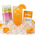 A Vinka cocktail base packet, a U-Fizz orange soda mix packet, and a tall glass of orange cocktail filled with ice, arranged on a bed of ice cubes with orange slices on a white background.