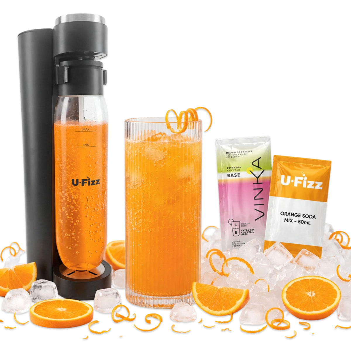 A U-Fizz carbonated drink maker setup on a white background, featuring a black carbonator machine, a glass of orange soda with ice, two Vinka orange soda mix packets, and scattered orange slices, ice cubes, and citrus peels.