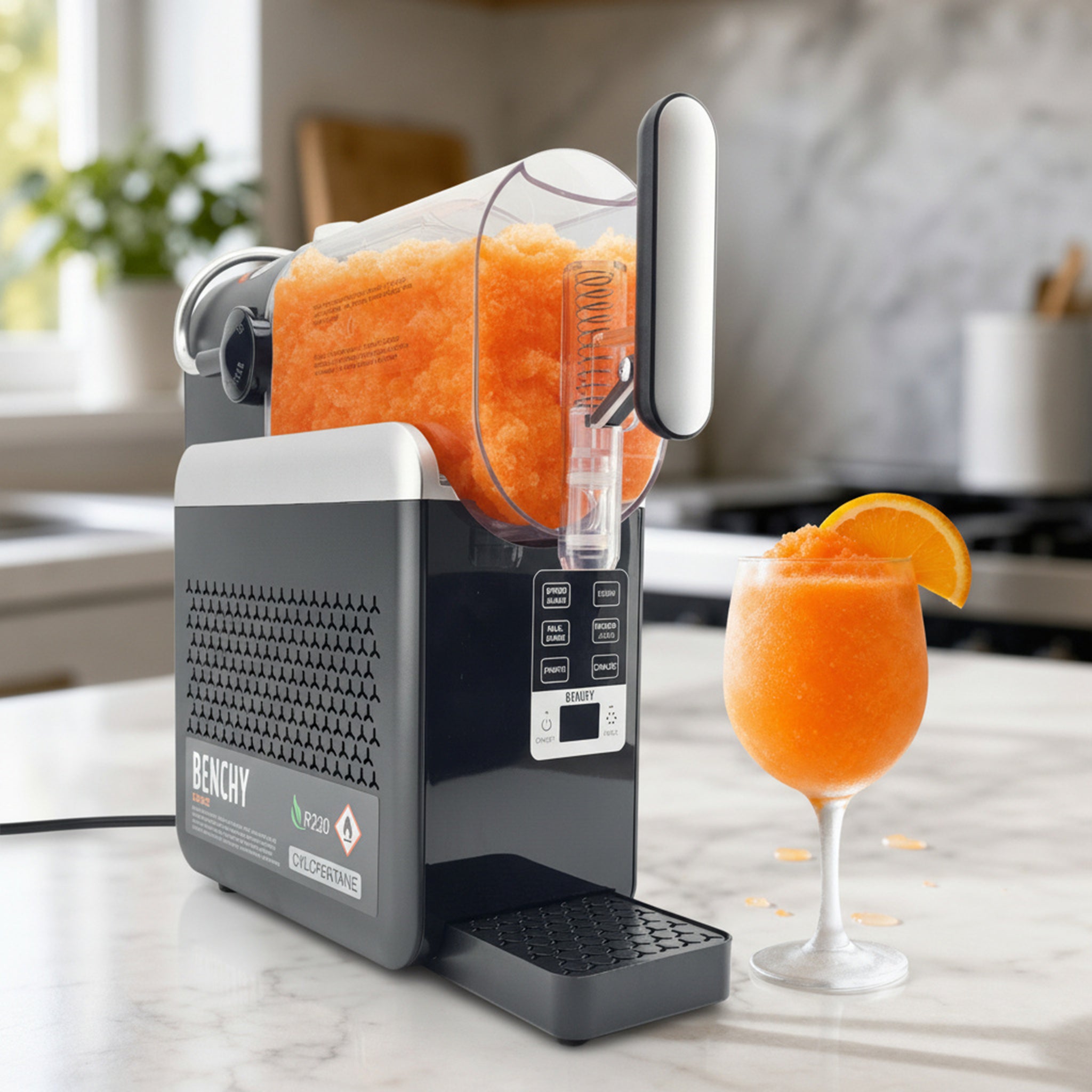 A BENCH Slushie Maker machine in black and silver, shown with an orange slushie in a stemmed glass on a marble countertop in a kitchen setting.