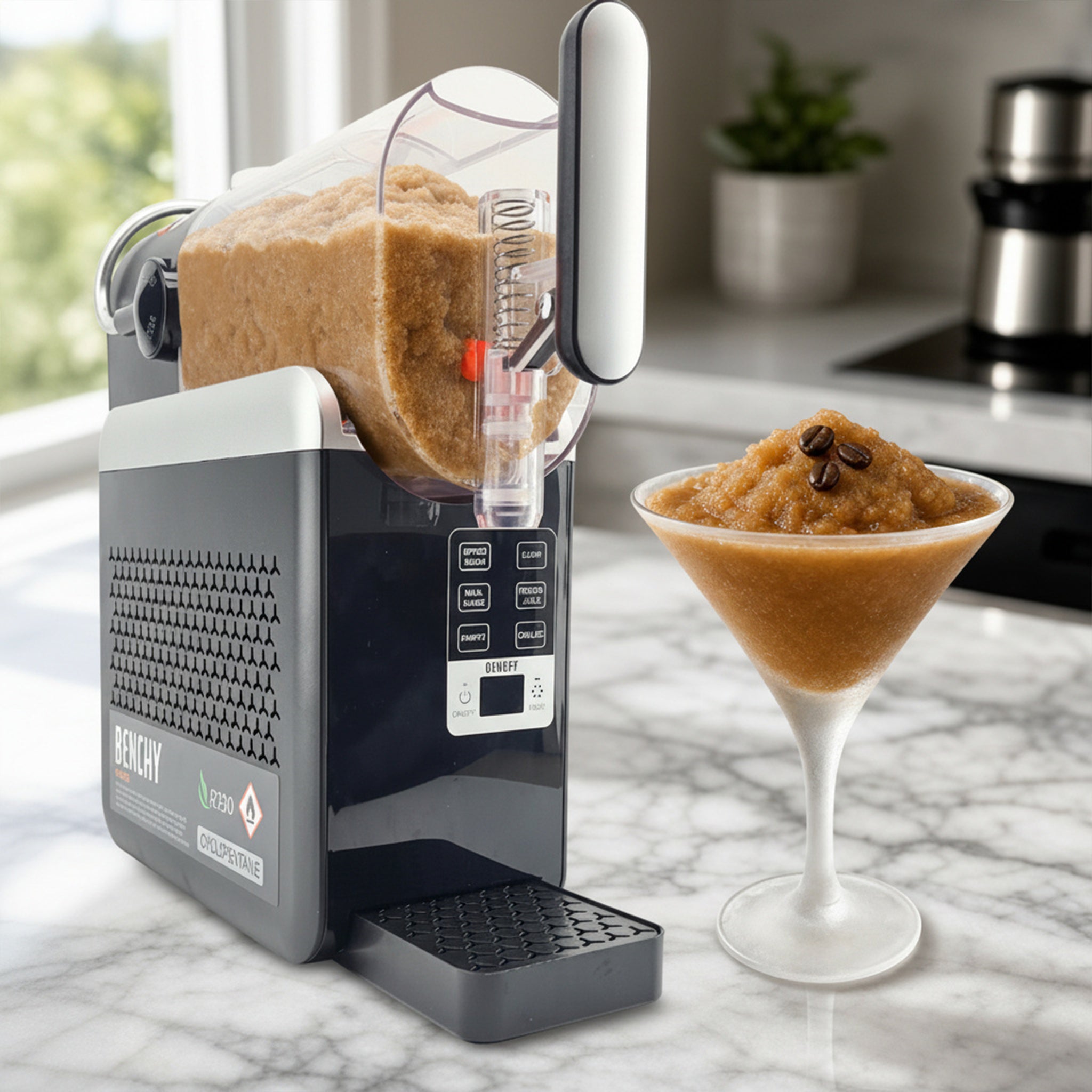 A Dolby Zulu Pro ice crusher and slushie maker shown on a marble countertop in a kitchen setting, with a clear container filled with slushie and a stemmed glass of slushie beside it.