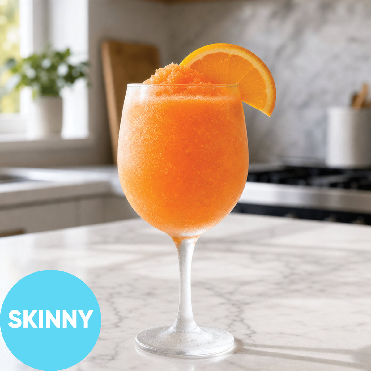 Frozen Skinny Aperitivo Spritz VINKA Slushy Cocktail Kit (2L) in a stemmed glass on a marble countertop, garnished with an orange slice, with a blue circle overlay reading 'SKINNY' in a blurred kitchen setting.