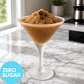 A Frozen Zero Sugar Espresso Martini (Frappe) VINKA Slushy Cocktail Kit (2L) in a martini glass on a marble countertop, with coffee beans on top and a blue circle reading ZERO SUGAR.