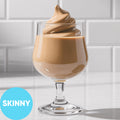 A clear stemmed glass filled with Frozen Skinny Hard Irish Cream VINKA Slushy Kit (2L), set on a white surface against a white subway-tile background. A bright blue circle in the lower left reads “SKINNY.