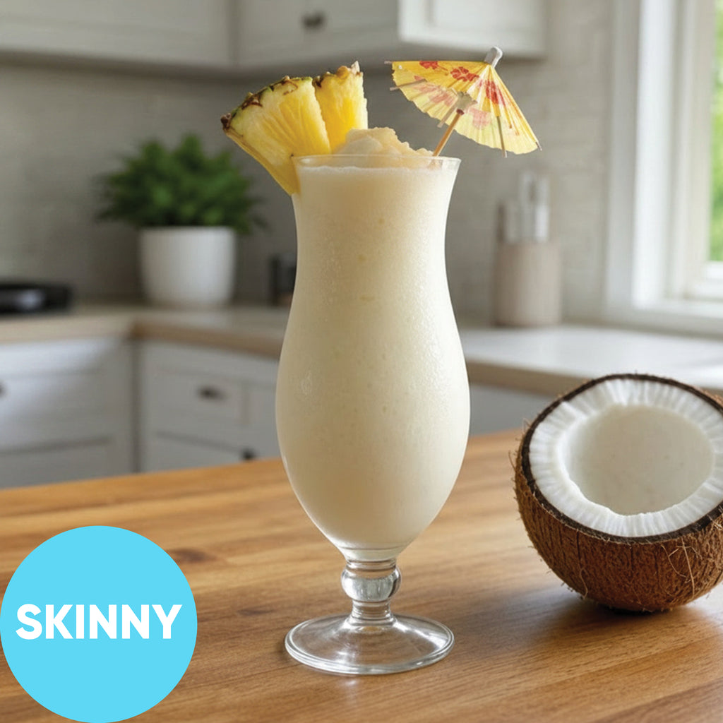 Frozen Skinny Pina Colada VINKA Slushy Cocktail Kit (2L) in a tall stemmed glass on a wooden table, garnished with pineapple slices and a small umbrella, with a half coconut beside it and a blue circle label reading SKINNY in the lower left.