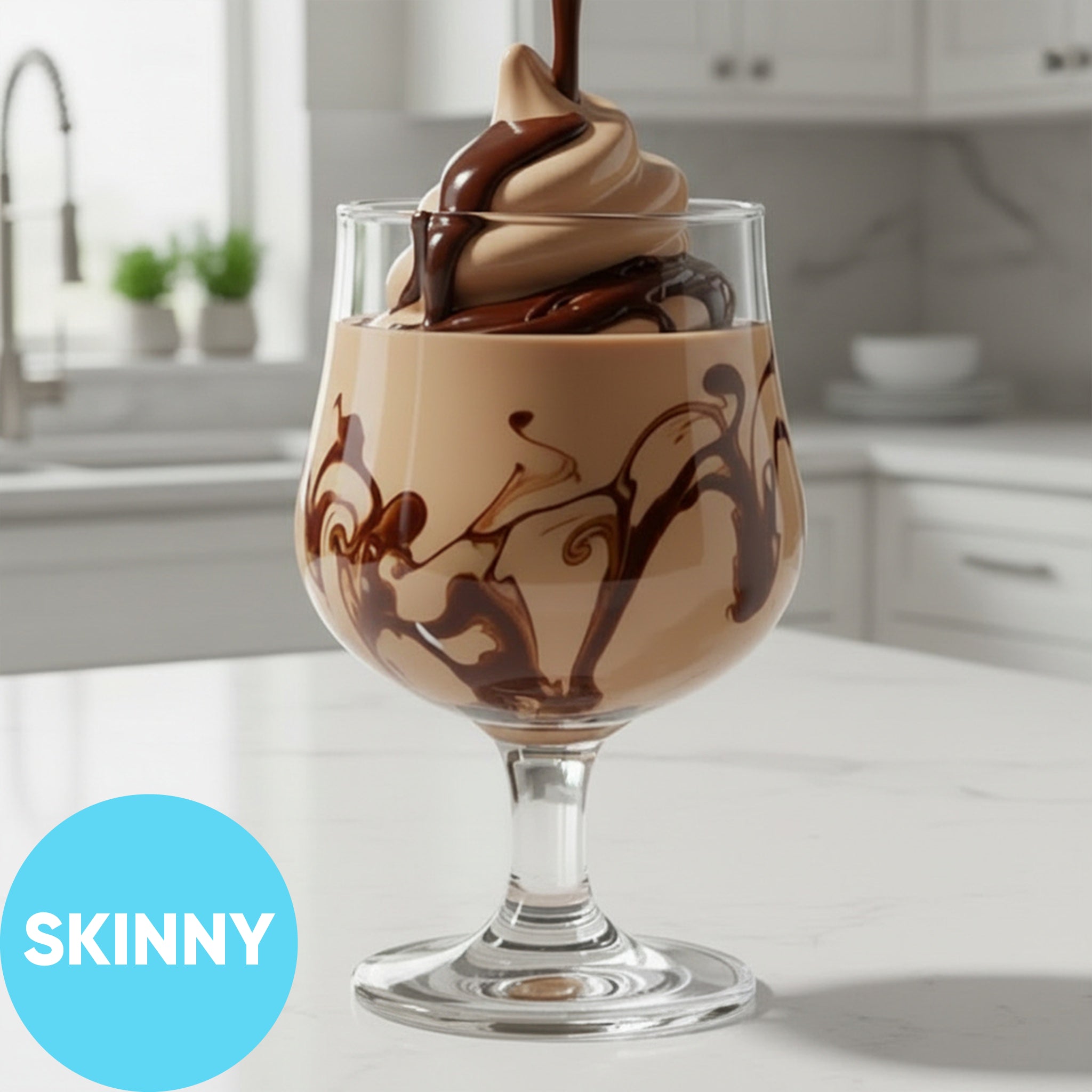 A clear stemmed dessert glass filled with Frozen Skinny Mudslide VINKA Slushy Cocktail Kit (2L), set on a white countertop in a bright kitchen. A blue circle in the lower left says SKINNY.