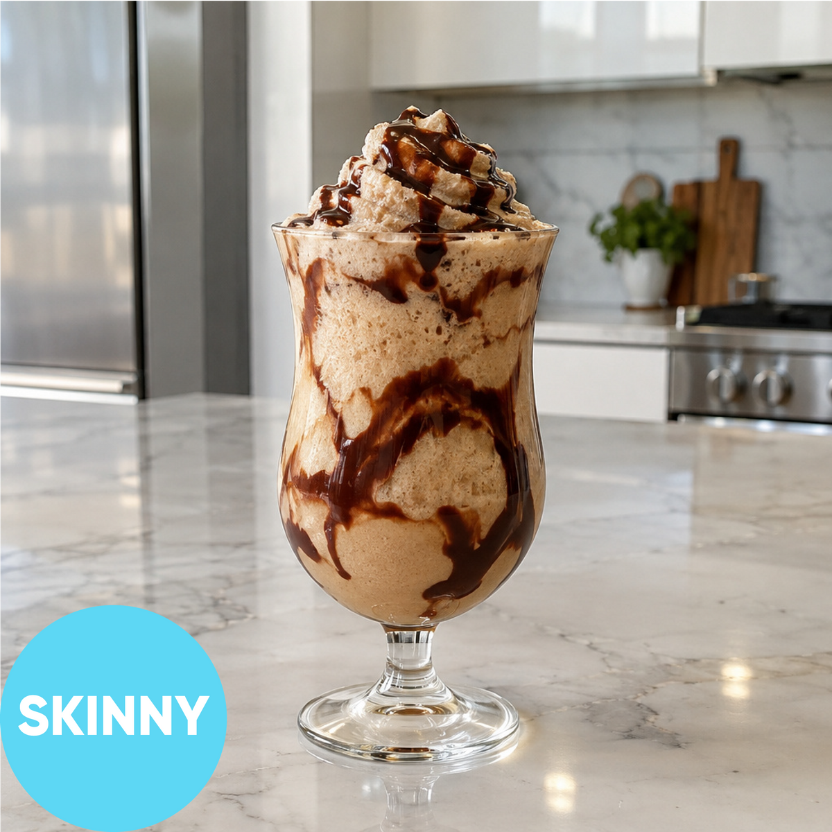 A tall glass filled with a light tan creamy dessert, topped with whipped cream and chocolate syrup, sitting on a marble kitchen counter. A blue circle in the lower left says 'SKINNY'.