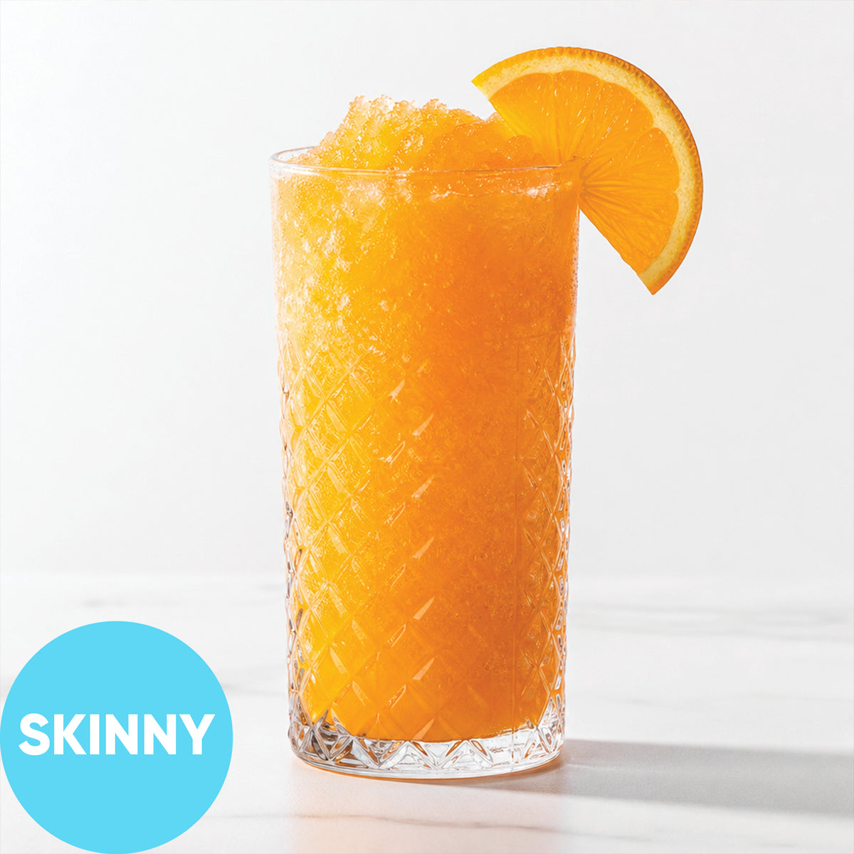 Frozen Skinny Hard Orange Soda VINKA Slushy Kit (2L) in a tall textured clear glass with an orange slice garnish, shown on a white background with a blue circular 'SKINNY' label in the lower left.