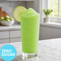 A tall clear glass filled withFrozen Zero Sugar Hard Sour Green Apple VINKA Slushy Kit (2L), garnished with a green apple slice, set on a kitchen counter with a blue circle label reading ZERO SUGAR.