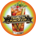 A clear glass cup filled with Trifecta Punch, strawberries, cucumber slices, orange slices, ice, mint, and a gold ribbon banner reading “TRIFECTA PUNCH CUP,” set on a cloth with strawberries and cucumber slices around it.
